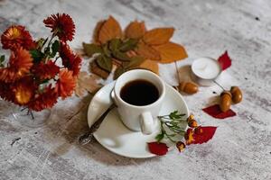 An aesthetic still life composition on a wooden backdrop showcasing a coffee cup, a spoon, and various seasonal elements like acorns and autumn leaves. photo