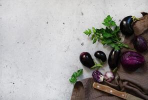 An aesthetic still life composition on a grey backdrop, highlighting eggplants and a bunch of fresh parsley, with a knife. photo