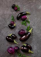 Close-up of a table arrangement with various eggplants and fresh parsley, with a knife placed on a textured, grey background. photo