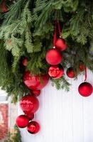 A small Christmas tree, decorated with red ribbons and standing in a silver bucket on a red stand, is displayed against a rustic, light-colored wooden fence. photo