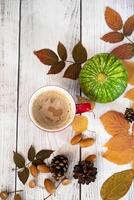 Close-up of a table arrangement with a coffee cup resting on a saucer, adorned with fallen leaves, acorns, a flower, and a candle to create an autumnal ambiance. photo