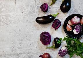 Overhead shot of a culinary arrangement with eggplants and a bunch of parsley, with a knife placed on a neutral, grey background. photo