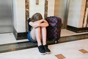 A woman sitting with a feeling of sadness and loss while traveling with a lot of luggage on the floor. The room is occupied. photo