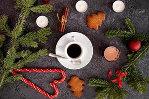 A festive flat lay featuring a cup of coffee, gingerbread cookies, cinnamon sticks, candy canes, candles, and pine branches on a dark, textured background. photo