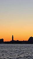 City skyline silhouette against a sunset over water, A serene view of a city skyline silhouetted against a warm sunset, with the calm waters in the foreground video
