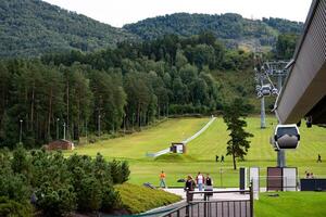 The image shows a scenic mountain landscape with a green grassy slope and a cable car system running up the hill. photo