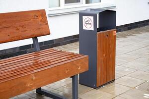 Wooden bench and trash bin with no smoking sign on a wet pavement. photo