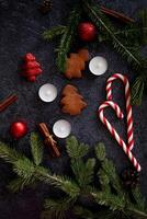 An aesthetic Christmas flat lay composition on a dark backdrop, highlighting a cup of coffee, gingerbread cookies, cinnamon sticks, candy canes, candles, and festive pine sprigs. photo
