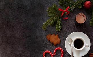 An artistic top shot of a Christmas decoration arrangement featuring coffee, gingerbread cookies, cinnamon sticks, candy canes, candles, and pine sprigs placed on a dark textured surface. photo