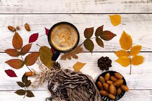 Close-up of a table arrangement with a coffee cup, red macarons, flowers, autumn leaves, acorns, and a candle, creating an autumnal ambiance. photo