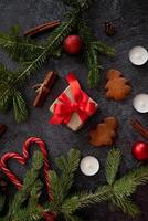 A festive flat lay featuring Christmas decorations, including a gift with a red ribbon, gingerbread tree cookies, cinnamon sticks, pine branches, candles photo