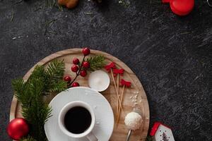 A comforting image of a coffee cup surrounded by Christmas treats and decorations, including gingerbread cookies, cinnamon sticks, candy canes, and candles, on a dark, festive background. photo