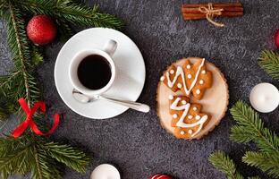 Close-up of a Christmas table arrangement with a coffee cup, gingerbread cookies, cinnamon, candy canes, candles, and pine branches creating a festive ambiance. photo