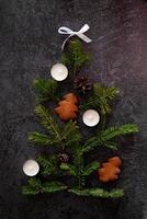 Overhead shot of a Christmas-themed arrangement with a gift box tied with a red ribbon, gingerbread cookies, cinnamon, pine sprigs, candles, candy canes photo