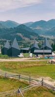 Unique Black Cabins with Cone Roofs in Open Field. A collection of distinctive black cabins with steep cone-shaped roofs, set in a grassy open field against a video