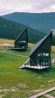 Aerial Modern A-Frame Cabins on Grassy Hillside. A group of modern black A-frame cabins with sharp architectural lines, video