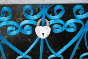Heart-shaped lock on the fence on the background of other castles, water, concrete pavement photo