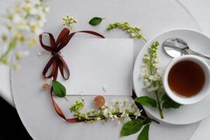 Scattered white flowers and soft green leaves surround a steaming cup of tea, highlighting the contrast between the warm beverage and the cool, fresh floral elements. photo