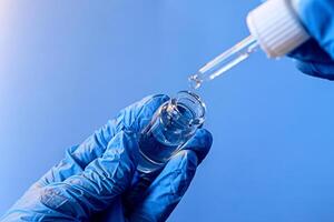 Dropping liquid from a pipette into a glass vial while wearing blue gloves in a laboratory setting photo