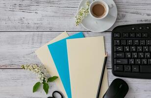 Workspace setup with coffee cup, notebook, pencil, and keyboard on wooden table photo
