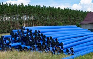 Stacked blue pipes resting in a field near a forest during daylight photo