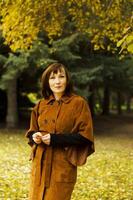 She is posing among trees with vibrant green leaves, indicating it might be early autumn. photo