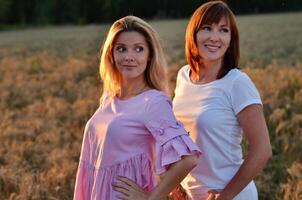 The woman on the right is dressed in a white top underneath an open, short-sleeved orange shirt, complemented by white pants. photo