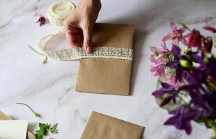 The bouquet consists of fresh-looking flowers with vibrant pink petals and yellow centers, adding a pop of color against the muted background of the wooden surface and craft paper. photo