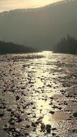 Serene River Flowing Through Misty Valley, A tranquil river reflecting soft sunlight, surrounded by bare trees and misty hills under a calm, overcast sky. video