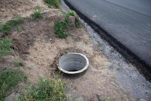 Drainage hole beside a newly paved road surrounded by grass and dirt photo