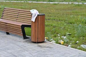 Wooden bench and trash can in a park with litter scattered around on the grass. photo