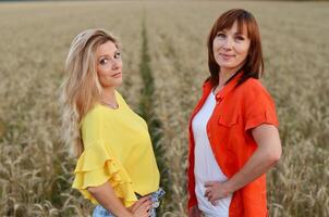 Two women are standing side by side in a wheat field, posing confidently with their hands on their hips. photo