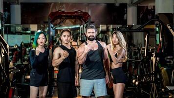 Confident diverse fitness team standing strong together in gym, raising fists as a symbol of unity, empowerment, and motivation for healthy lifestyle and teamwork. photo