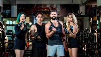 Diverse group of fit individuals lifting dumbbells in gym, confidently posing together in strength and unity, representing health, motivation, and teamwork. photo
