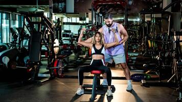 Personal trainer guiding female client through seated dumbbell shoulder press exercise in gym, focusing on proper form and strength training technique photo