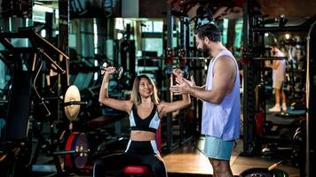 Female fitness client smiling while lifting dumbbells during seated shoulder press with supportive personal trainer coaching in modern gym setting photo