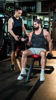 Personal trainer assisting man with seated dumbbell bicep curls at gym, emphasizing proper technique, strength training, and fitness motivation for muscle growth. photo