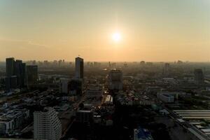 Scenic aerial view of a modern city skyline at sunset with golden sunlight illuminating tall buildings, roads, and urban landscape under a hazy evening sky photo