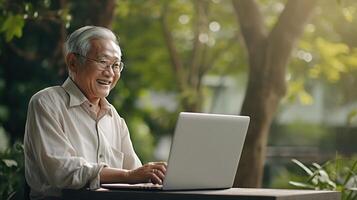 An older man sitting in a park using a laptop photo