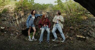 Three friends are smiling and talking standing near a ruined historical building. The man smokes. A sunny summer day photo