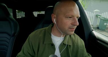A man with earphones gathers his things and gets out of the car. Front view from the car interior. Summer day photo