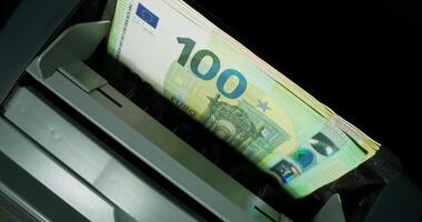 The calculating machine counts banknotes in denominations of one hundred and two hundred euros, standing on a black background. Close-up photo