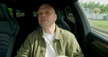A man with earphones drives a car with a concentrated look. He drinks from a bottle. Front view from the car interior. Summer day photo