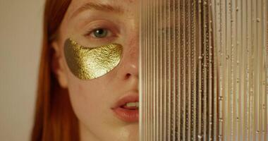 A woman with an eye patch looks at the camera with a serious look. Half of her face is covered with glass with water running down it. Studio photo
