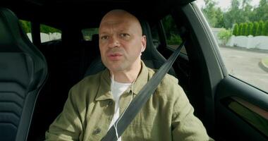 A man talks on earphones with a serious look when driving a car. Front view in the car interior. Summer day photo