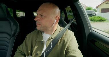 A man talks on earphones with a serious look and drinks from a bottle when driving a car. Front view in the car interior. Summer day photo