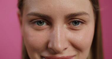 A woman smiles while looking at the camera standing on a pink studio background. Close-up of her face photo