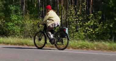 A woman rides a bicycle along the forest on a sunny day. Side view photo