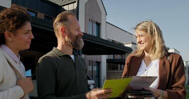 A realtor shows clients a booklet with a house design project while standing in the backyard. The family is going to buy a house photo