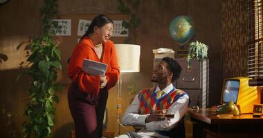 A man and a woman are talking in a retro office. A man is sitting in an armchair with a cup of coffee. A woman with documents stands in front of him photo